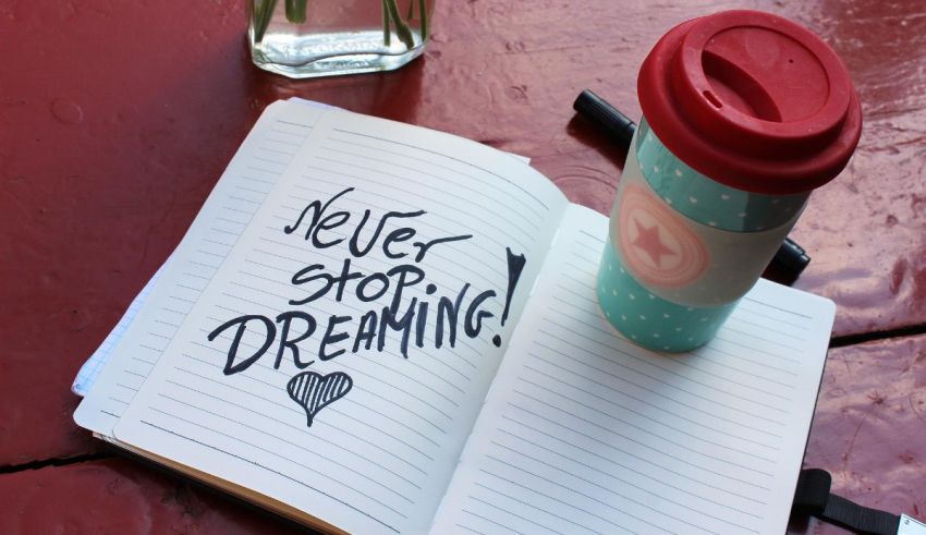 A notebook with the words never stop dreaming next to a cup of coffee.
