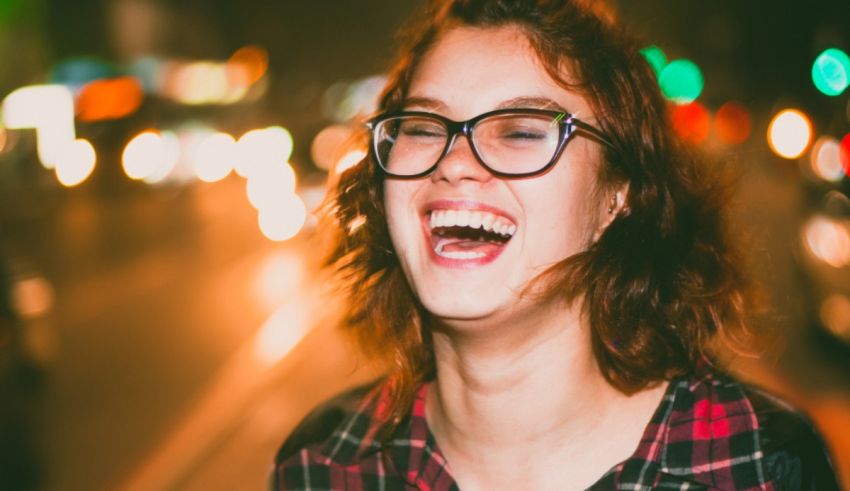 A woman wearing glasses is laughing in a city at night.