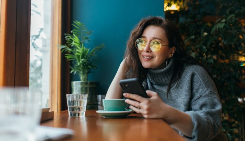 A woman is sitting at a table with a cup of coffee and a cell phone.