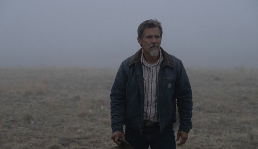 A man in a jacket standing in a field with a hat.