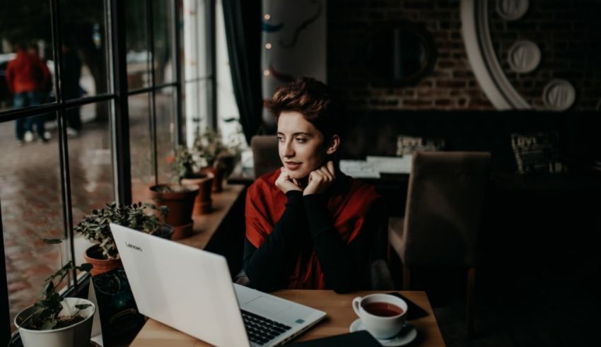 A woman sitting at a table with a laptop in front of a window.