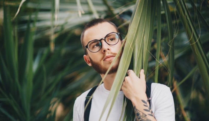 A man in glasses is hiding behind a palm tree.