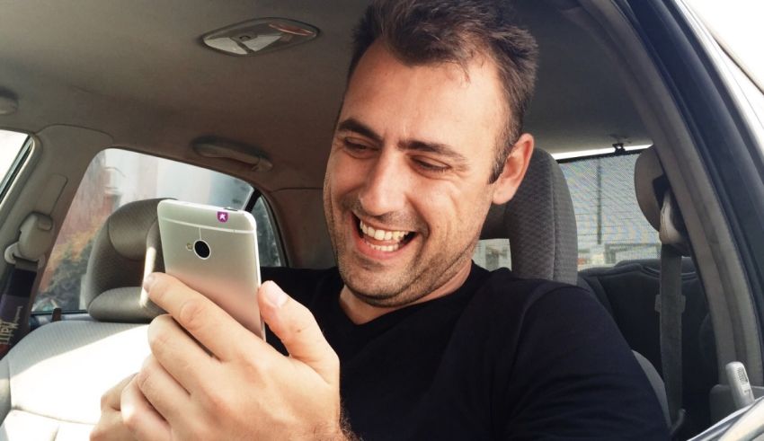 A man is smiling while using his cell phone in a car.