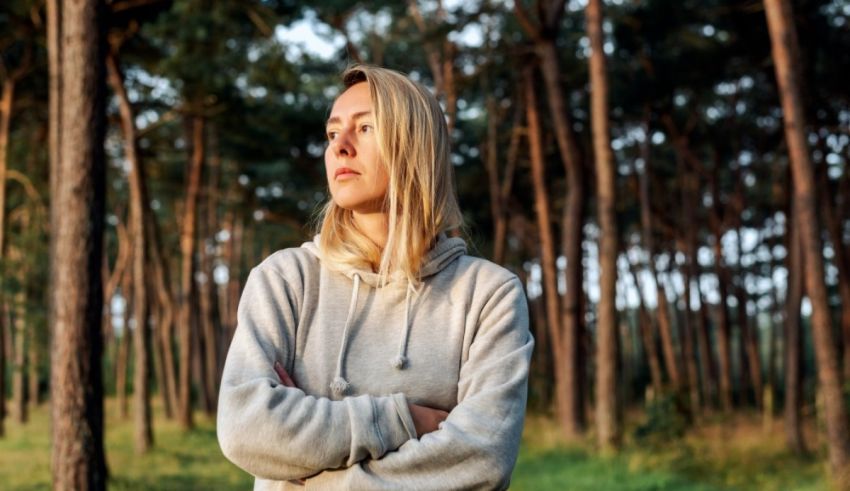 A woman standing in a forest with her arms crossed.