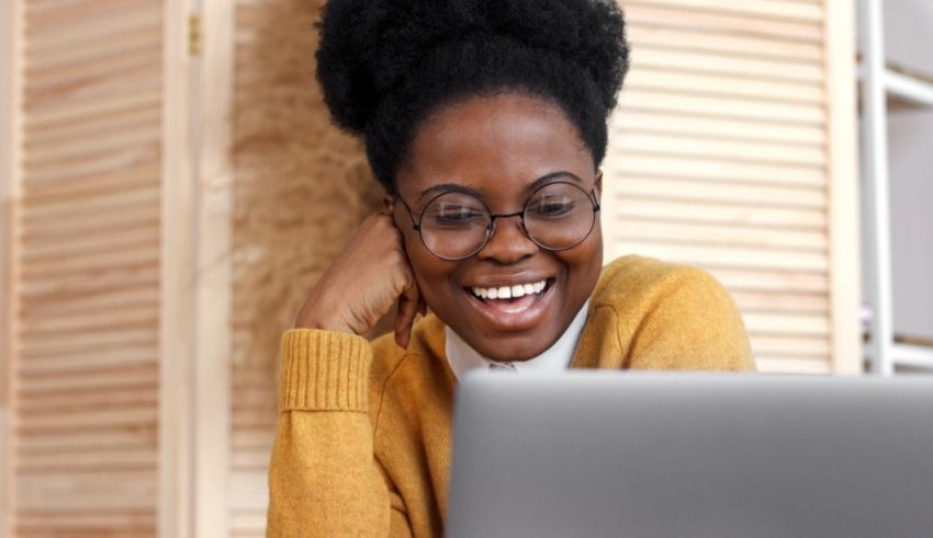 A young black woman smiling while using a laptop.