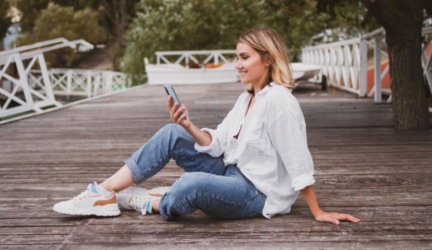 A young woman sitting on a wooden deck and using a cell phone.