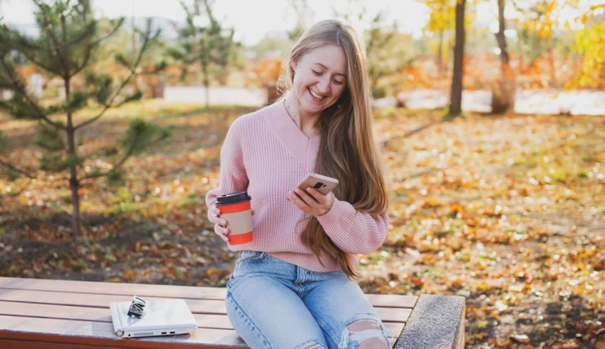 A girl sitting on a bench with a cup of coffee and a cell phone.