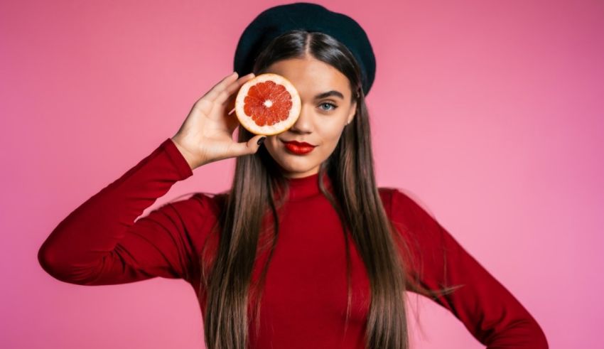 A young woman holding a grapefruit in front of her face.