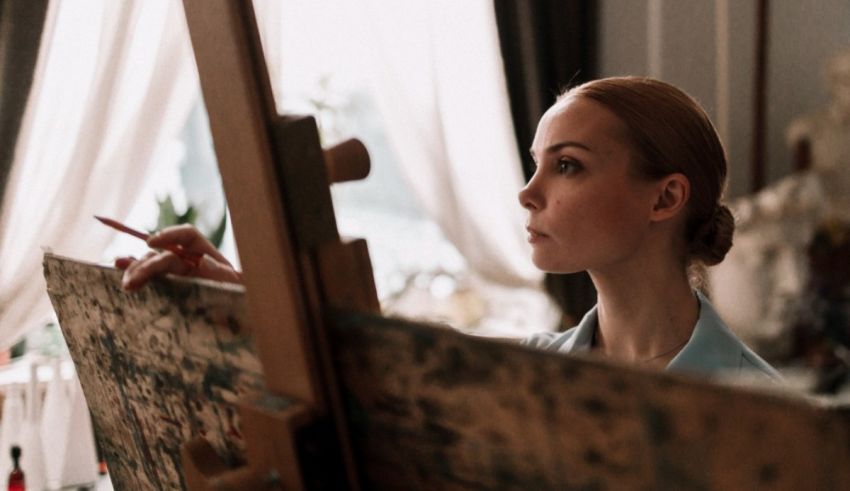 A woman is painting on an easel in front of a window.