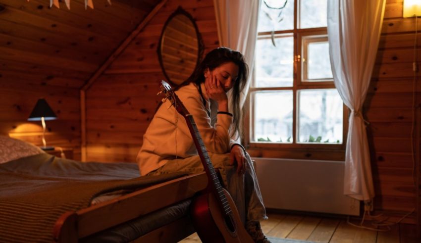 A woman sitting on a bed in a cabin with an acoustic guitar.