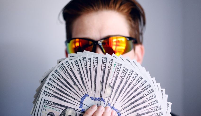 A man in sunglasses holding up a bunch of dollar bills.