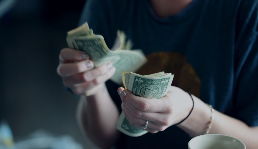 A woman is holding money in front of a coffee cup.