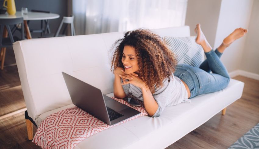 A young woman laying on a couch and using a laptop.