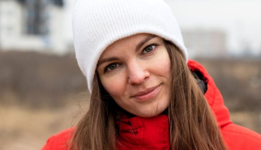 A young woman wearing a red jacket and white beanie.