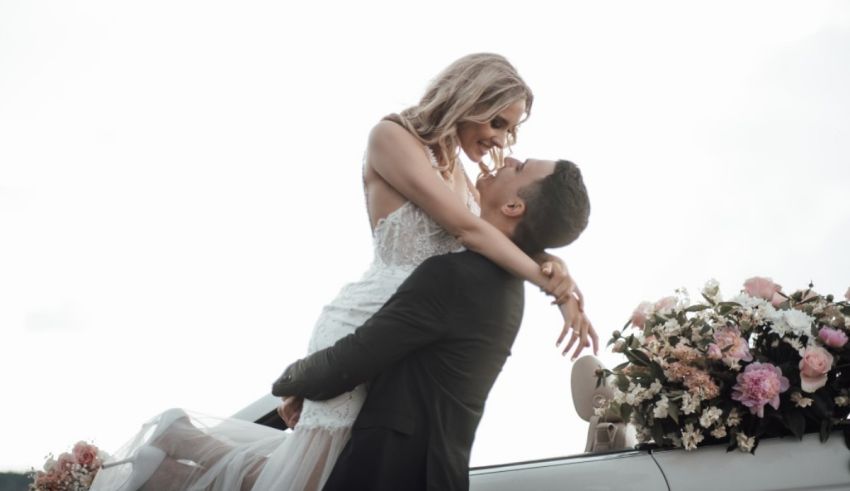 A bride and groom kissing in front of their wedding car.