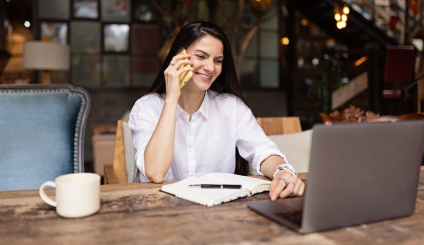 A woman talking on the phone while sitting at a table with a laptop.