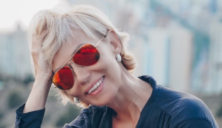 A woman with red sunglasses is smiling in front of a city.