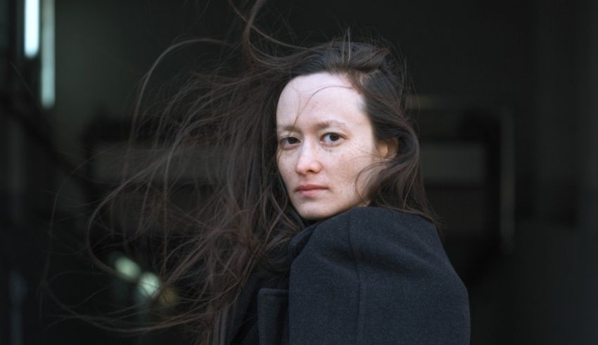 A woman in a black coat with hair blowing in the wind.