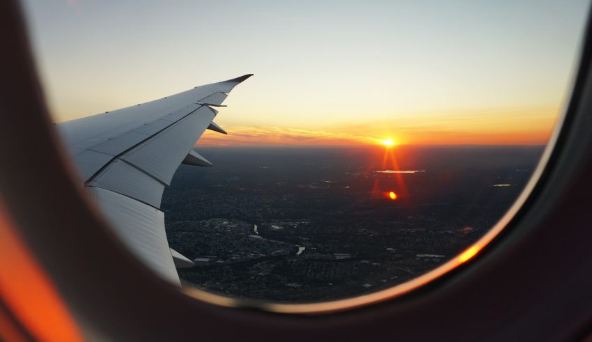 An airplane wing is seen through a window at sunset.