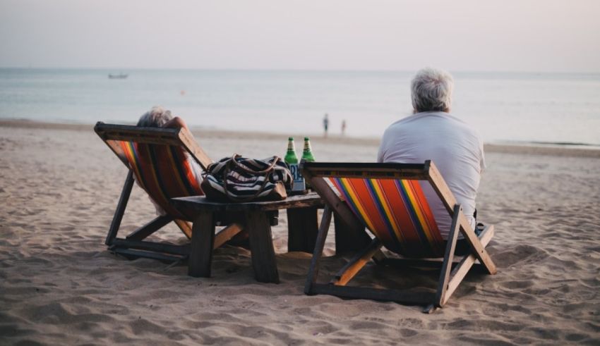 Two elderly people sitting in deck chairs on the beach.