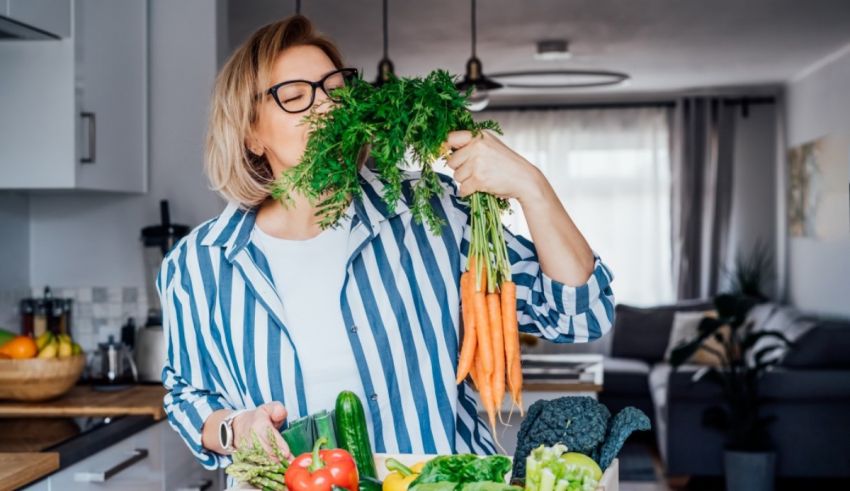 A woman in glasses is holding a box of vegetables in her kitchen.