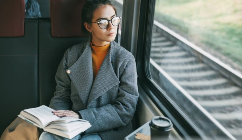 A woman is sitting on a train reading a book.
