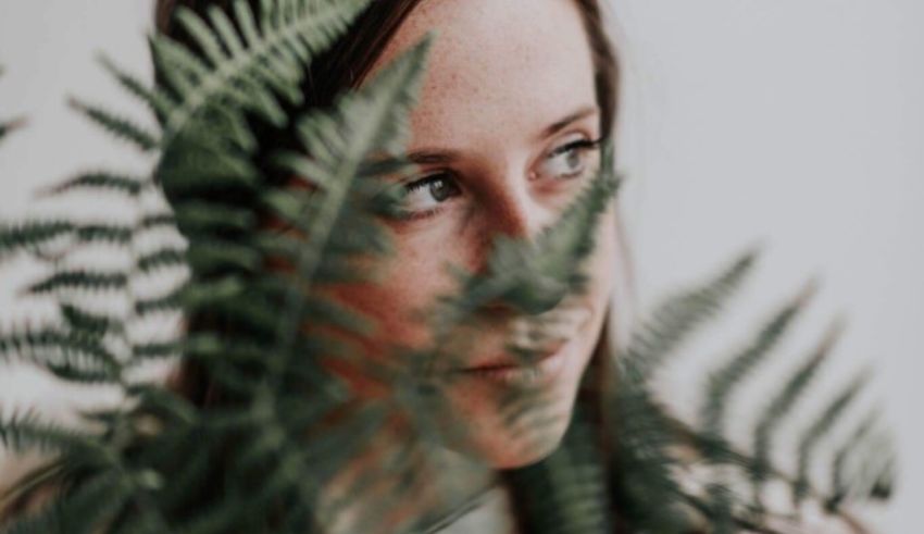 A woman's face peeking out from behind a fern.