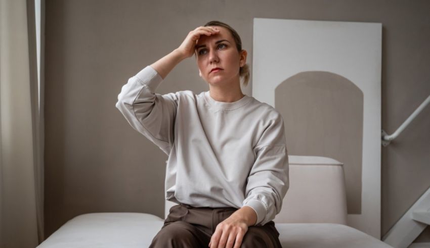 A woman sitting on a bed with her hand on her head.