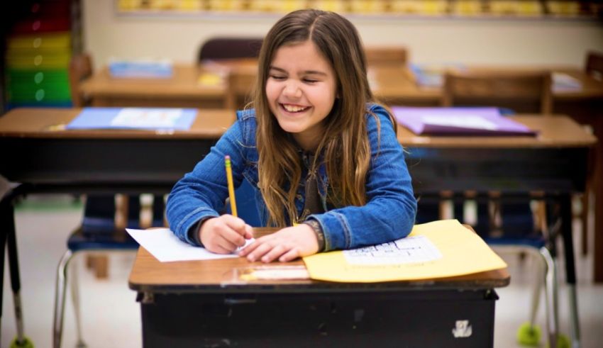 A girl sits at a desk and writes on a piece of paper.