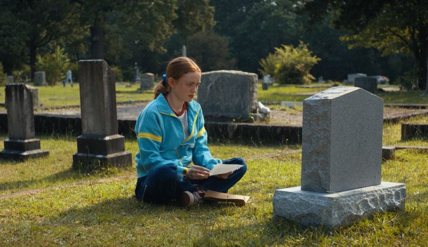 A woman sitting on the ground reading a book in a cemetery.