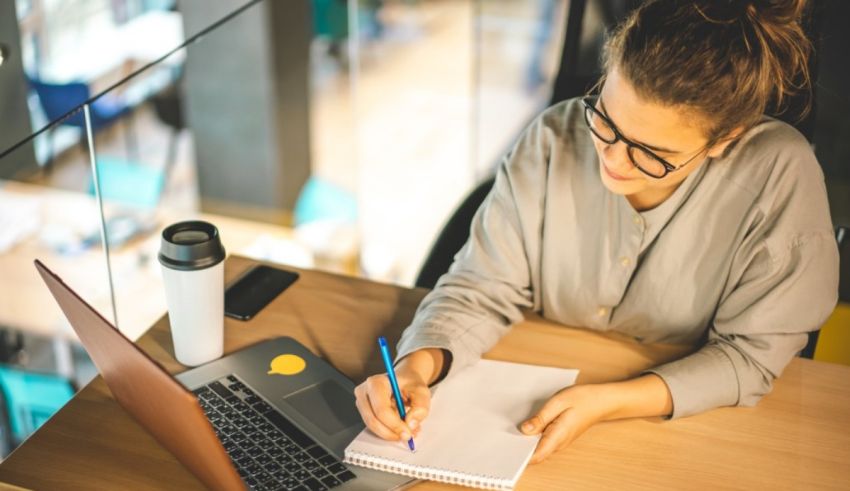 A woman writing in a notebook at a desk.