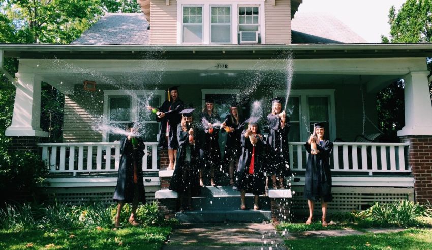 A group of graduates spraying water on each other in front of a house.