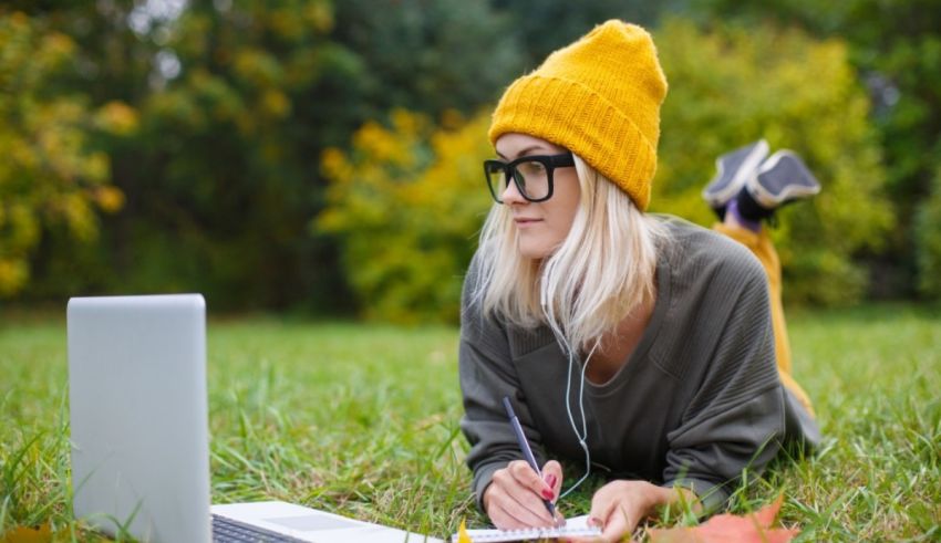 A young woman laying on the grass with a laptop.