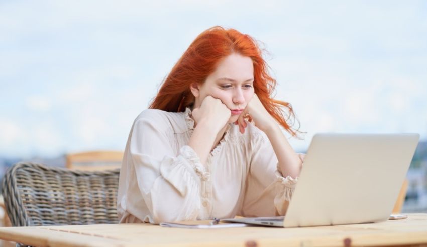 A woman with red hair sitting at a table with a laptop.
