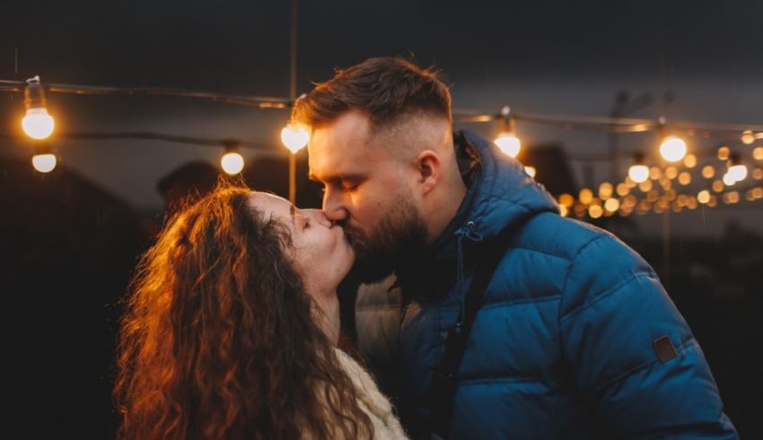 A couple kissing in front of a string of lights.