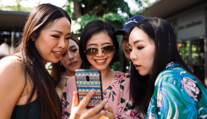 A group of asian women taking a picture with their cell phone.