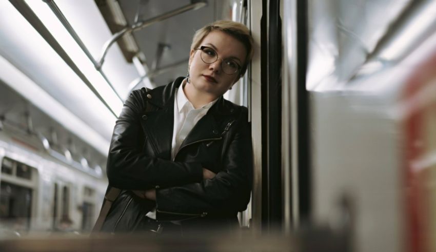 A woman in glasses is leaning against the side of a train.