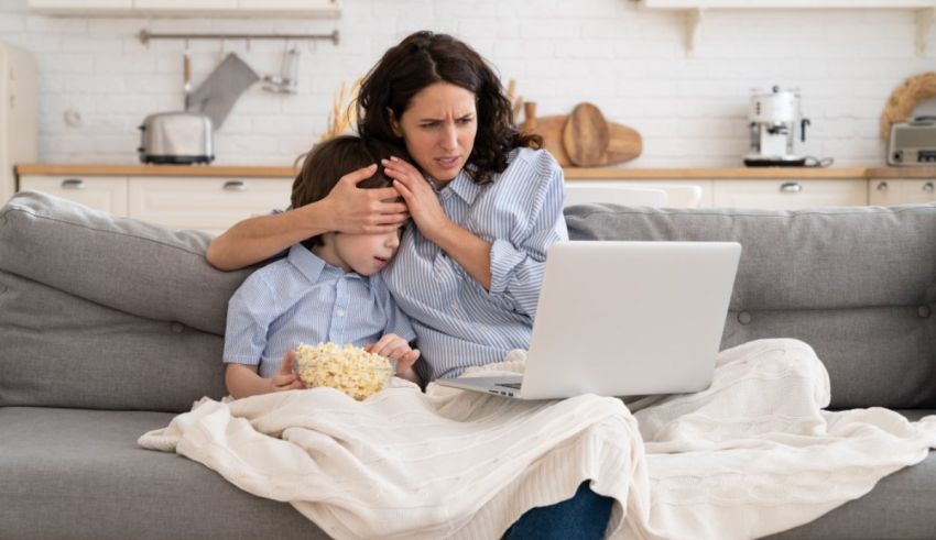 A woman and her son sitting on a couch with popcorn and a laptop.