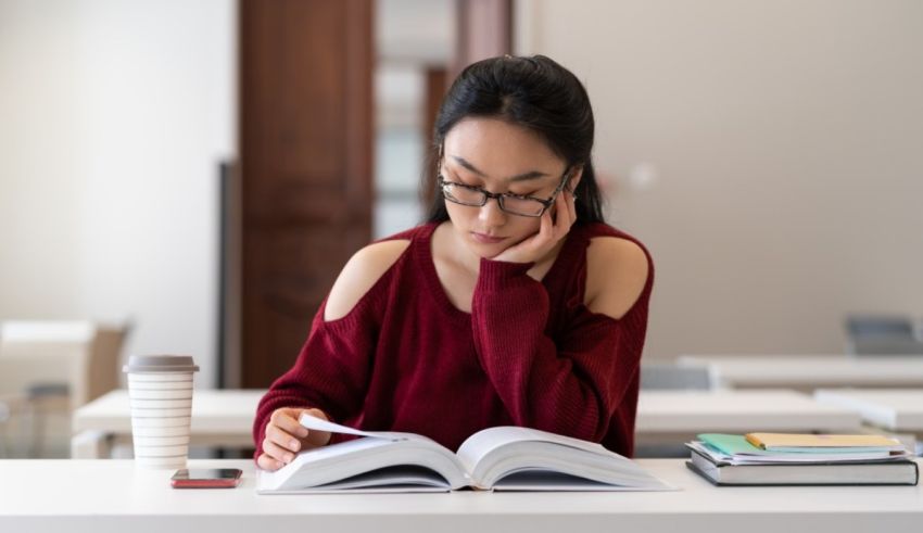 Asian female student reading a book in a classroom.