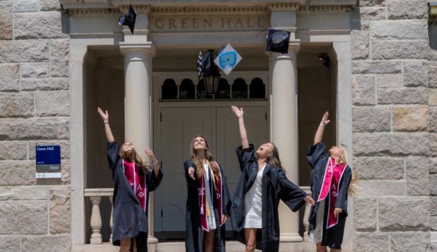 Four women in graduation gowns tossing hats in front of a building.