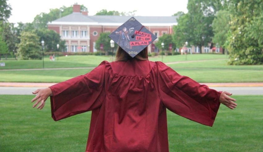 A woman in a graduation gown with her arms outstretched.