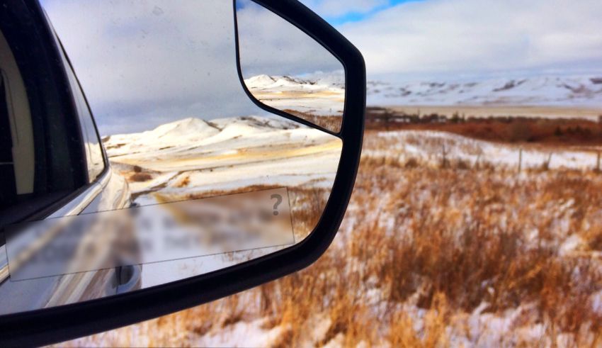 A side view mirror of a car with mountains in the background.