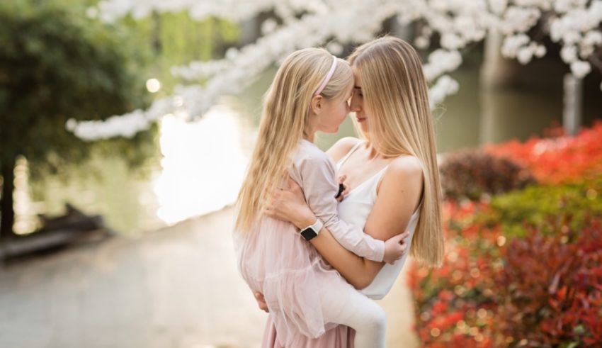 A mother and daughter hugging in front of a cherry blossom tree.