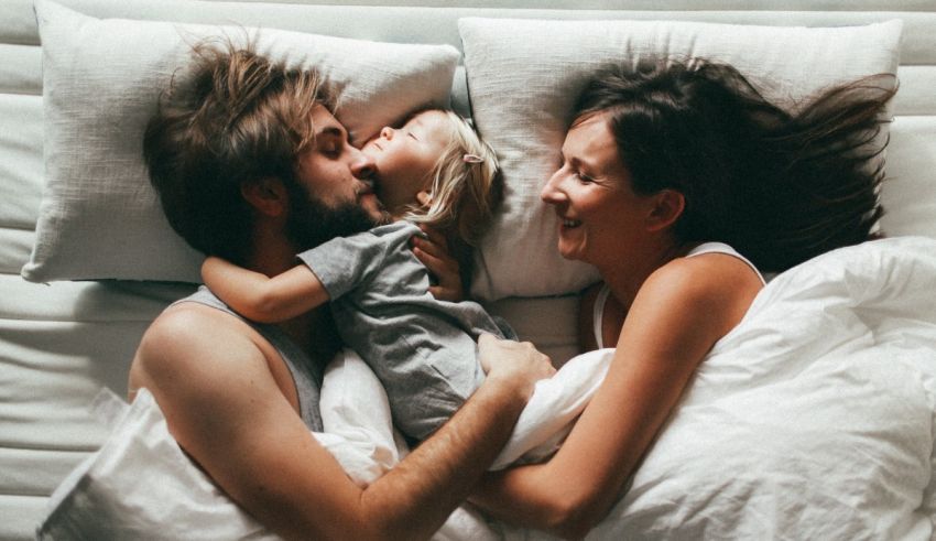 A man and woman hugging in bed with a child.