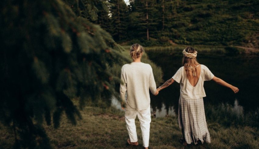 Two people holding hands near a pond in the woods.