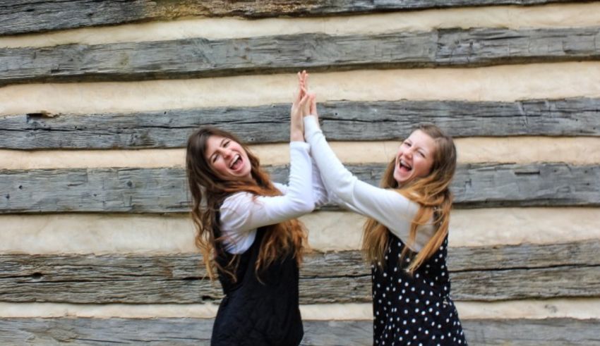 Two girls giving each other high fives in front of a log cabin.