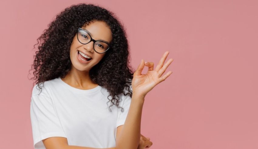 Young african american woman with glasses showing ok sign on pink background.