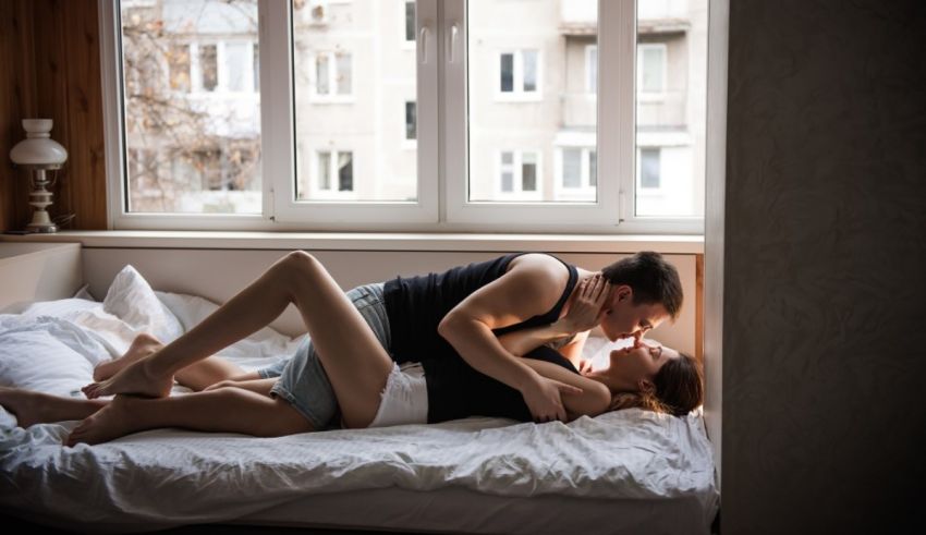 A man and woman laying on a bed in front of a window.