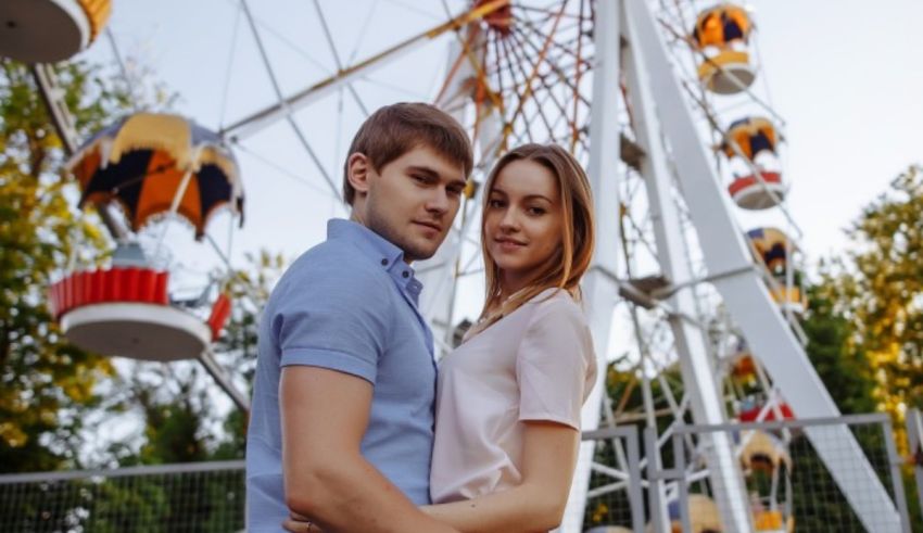 A young couple posing in front of a ferris wheel.