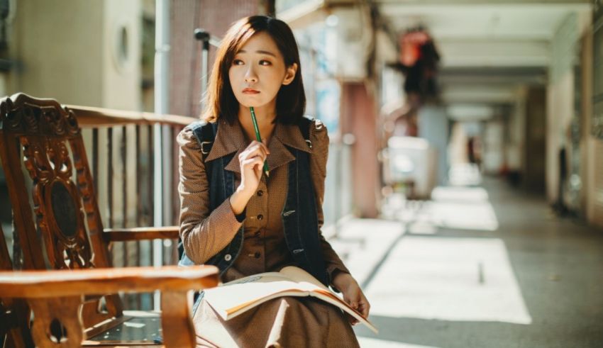 A young asian woman sitting on a bench reading a book.